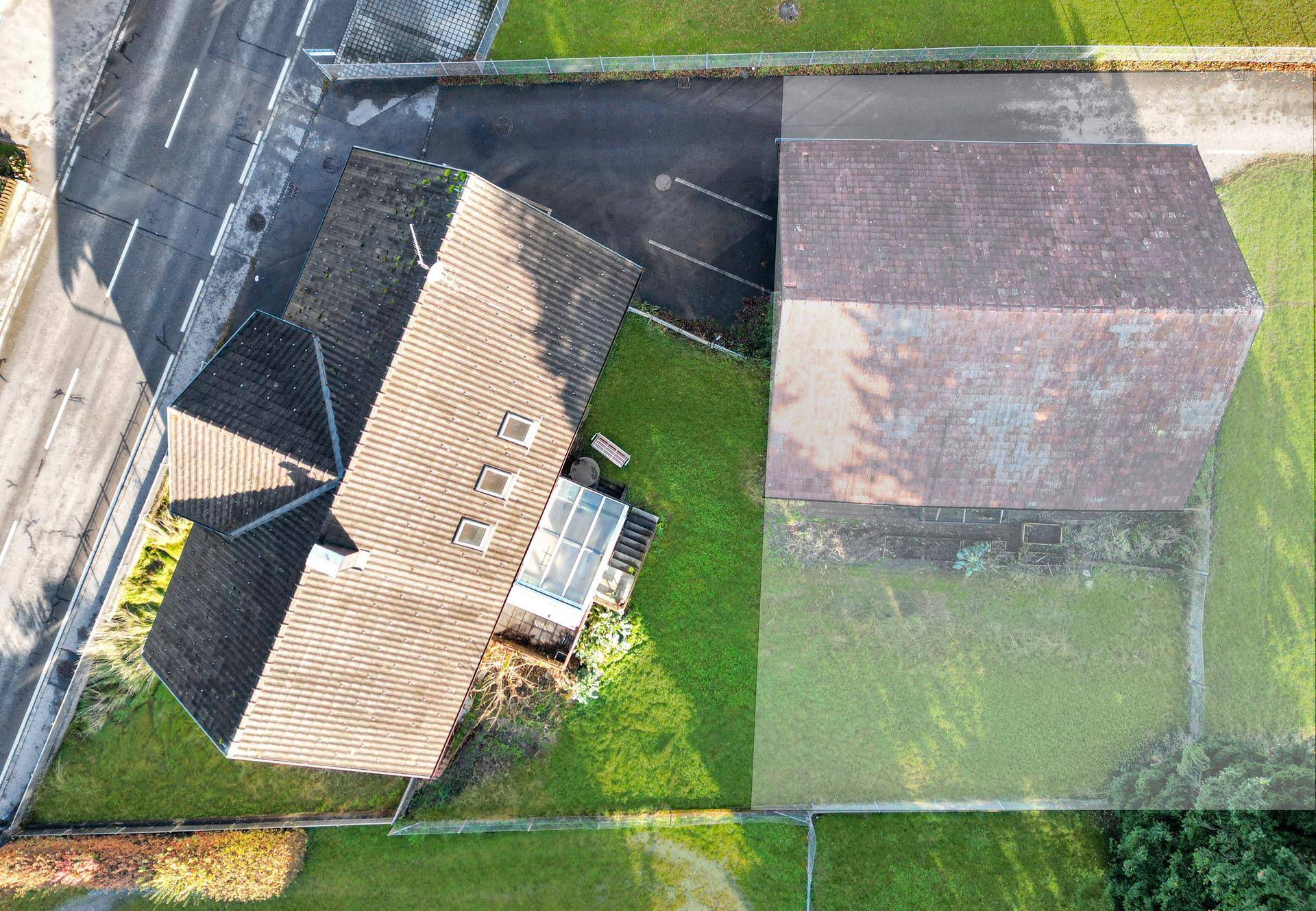 Draufsicht auf ein Wohnhaus und ein Holzgebäude mit umliegenden Grünflächen und Wegen.