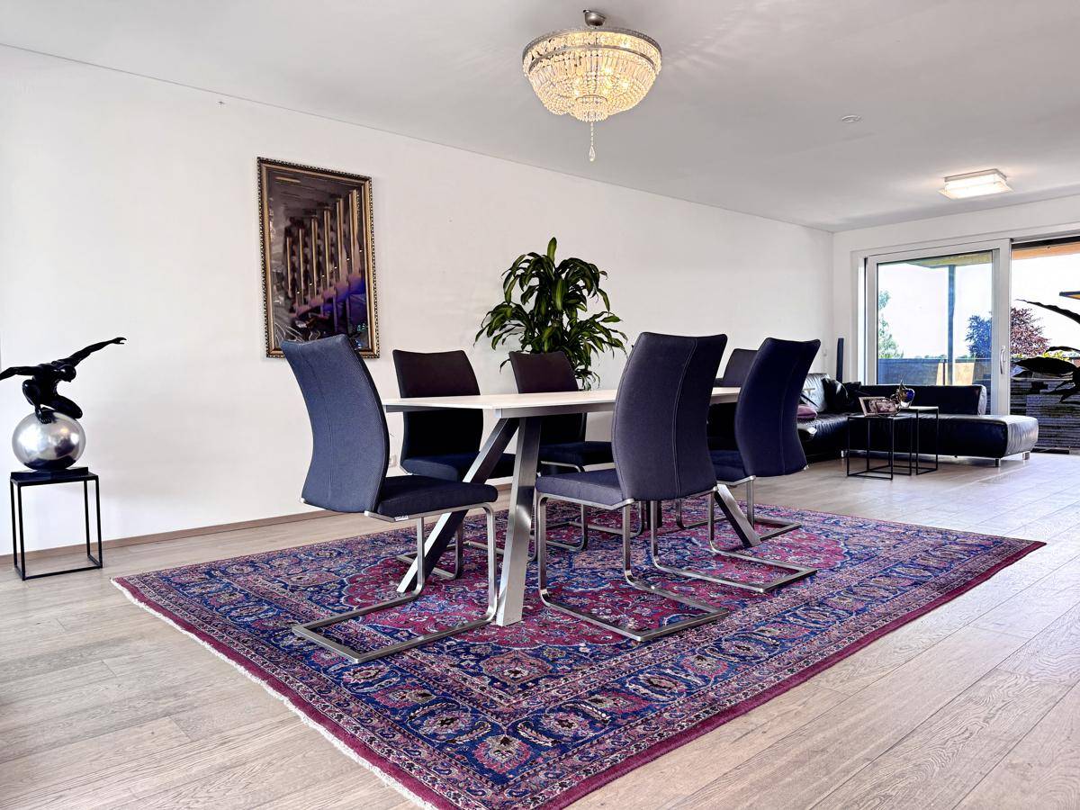 Eleganter Essbereich mit großem Tisch, modernen Stühlen und Kronleuchter über dem Teppich.