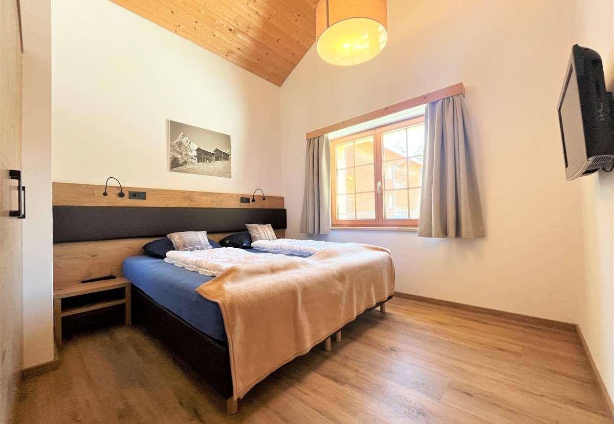Gemütliches Schlafzimmer mit Doppelbett, Holzboden und schräger Holzdecke, hell durch ein Fenster.