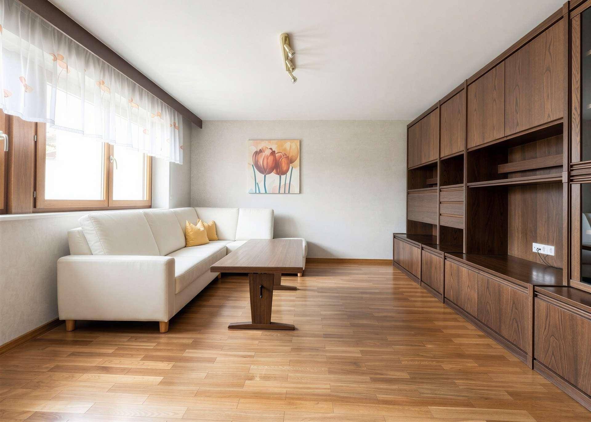 Gemütliches Wohnzimmer mit Holzboden, weißem Sofa und großer Holzschrankwand.