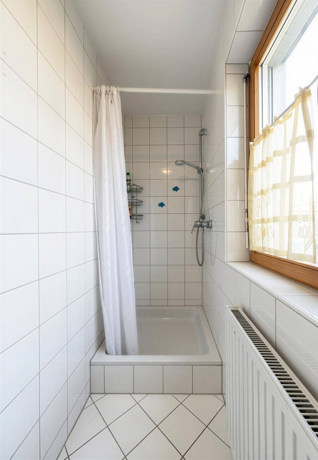 Helles Badezimmer mit Duschwanne, weißen Fliesen und Fenster.
