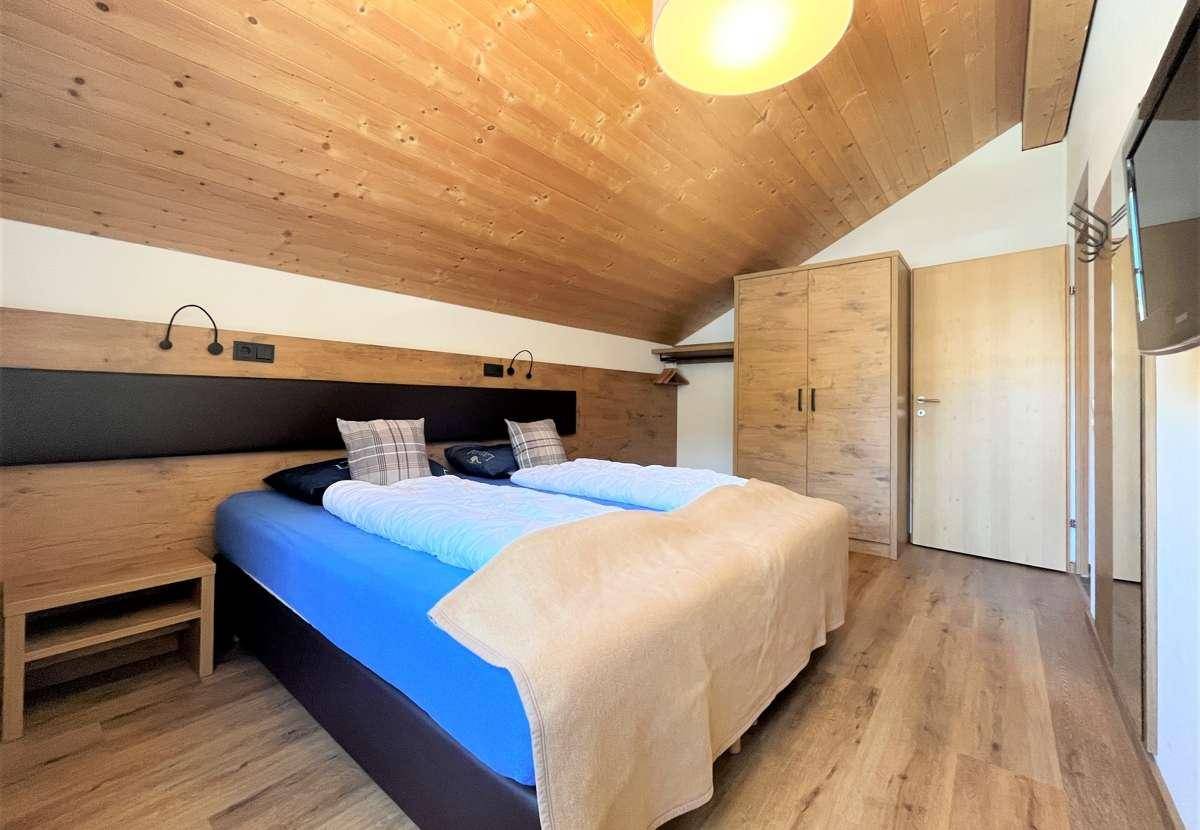 Schlafzimmer mit Holzboden, Kleiderschrank und schräger Holzdecke, bietet eine warme Atmosphäre.