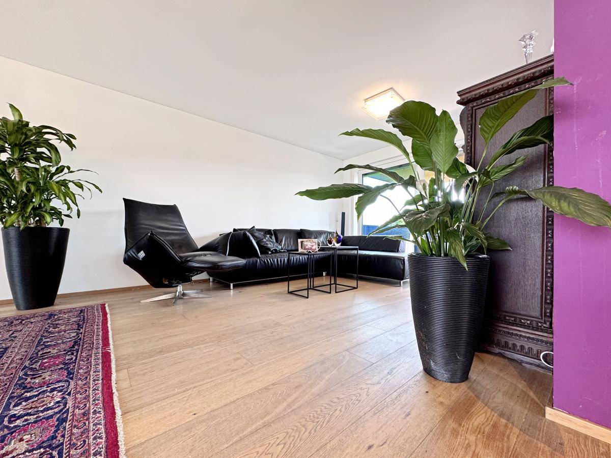 Gemütliches Wohnzimmer mit dunklem Ledersofa, Holzboden und dekorativen Pflanzen.