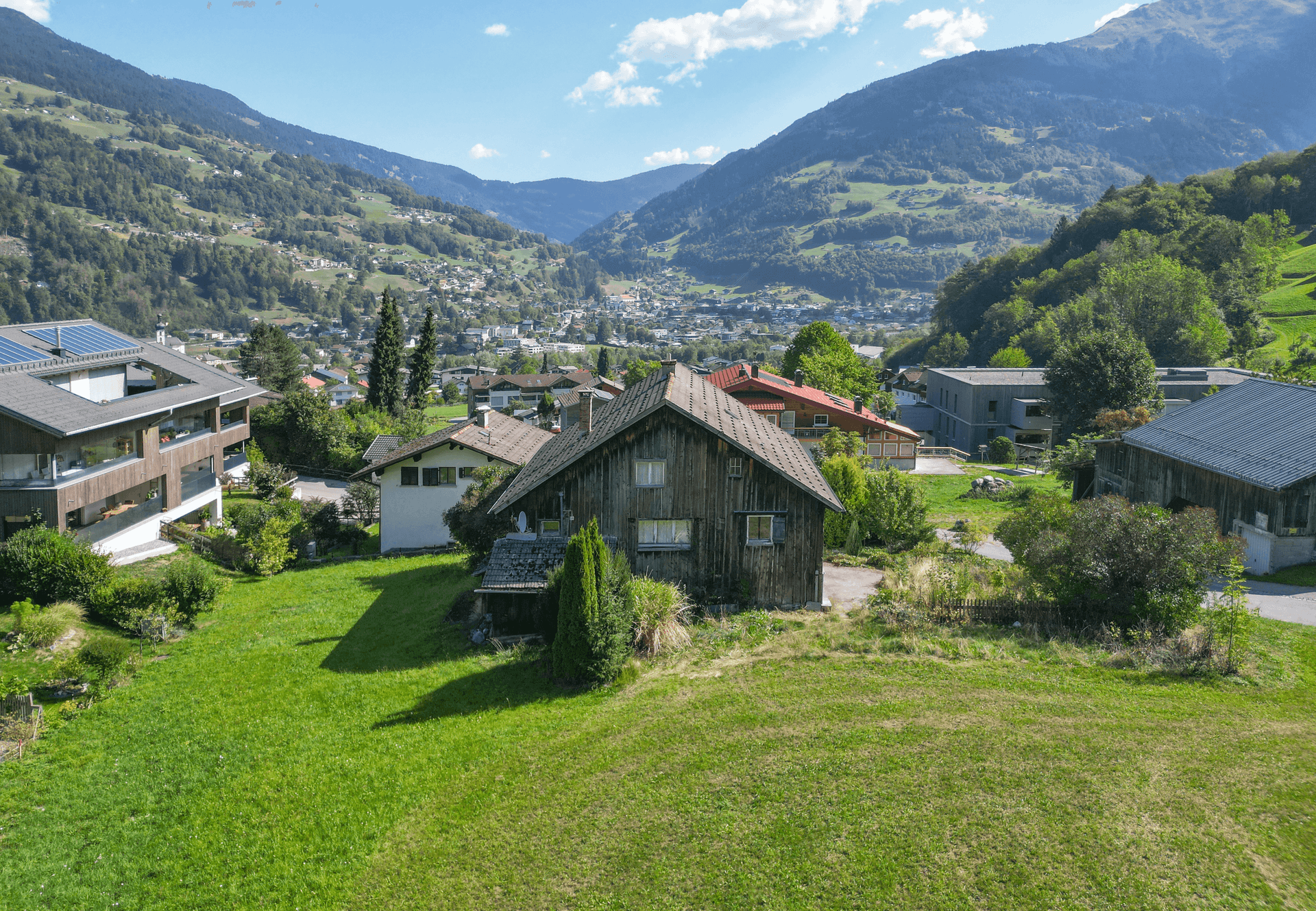 Haus in ländlicher Umgebung mit weitem Blick auf ein Tal und eine Siedlung, umgeben von grünen Hügeln.