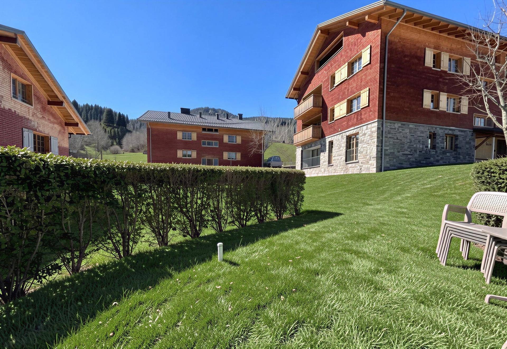Weitläufige Rasenfläche mit Hecke und traditionellen Gebäuden im Hintergrund unter blauem Himmel.