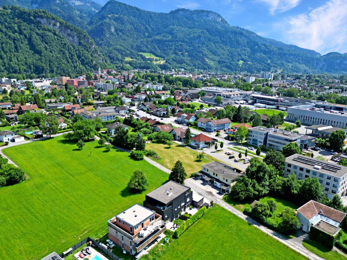 Weitläufige Luftaufnahme der Wohngegend mit viel Grün und Bergen im Hintergrund.