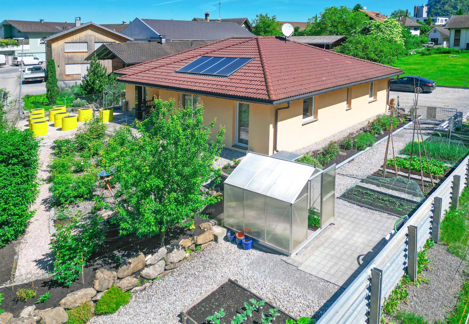 Luftaufnahme des Hauses mit großem Gemüsegarten, Gewächshaus und Solaranlage auf dem Dach.