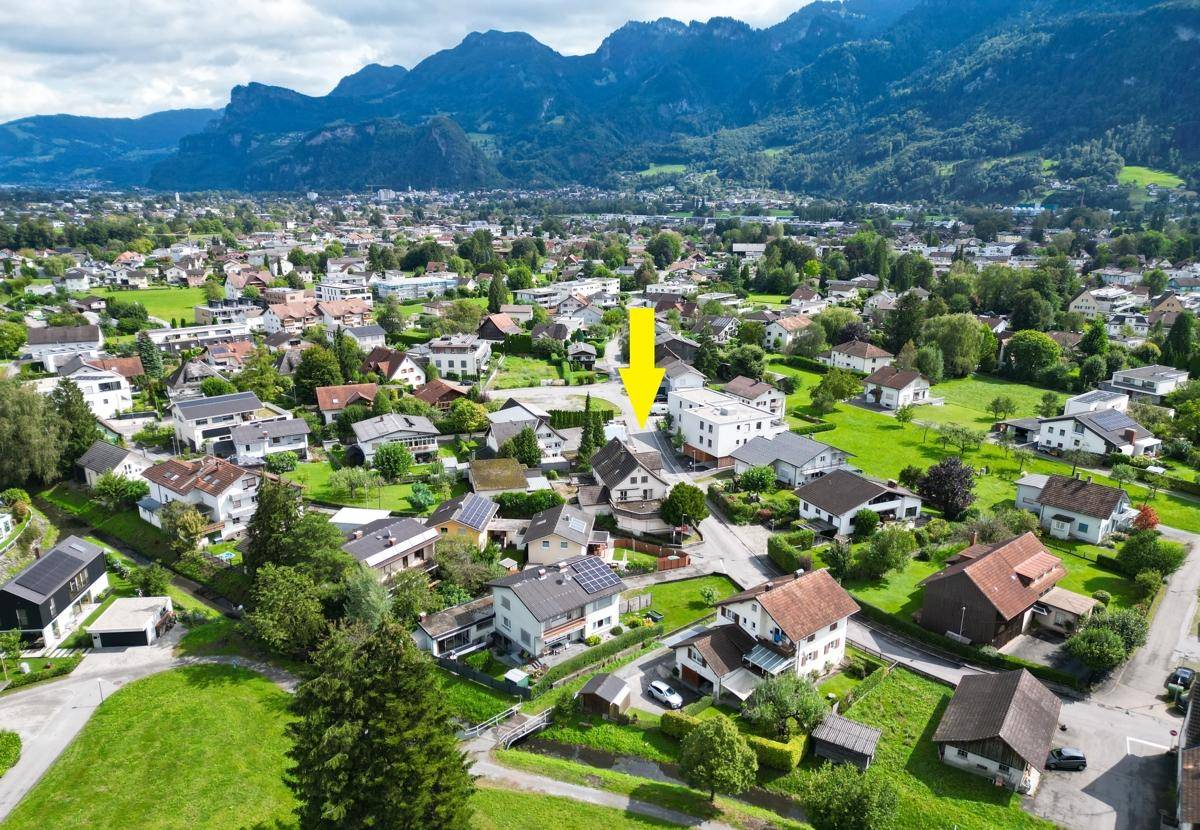 Luftaufnahme der Wohngegend mit markiertem Grundstück und beeindruckendem Bergpanorama.