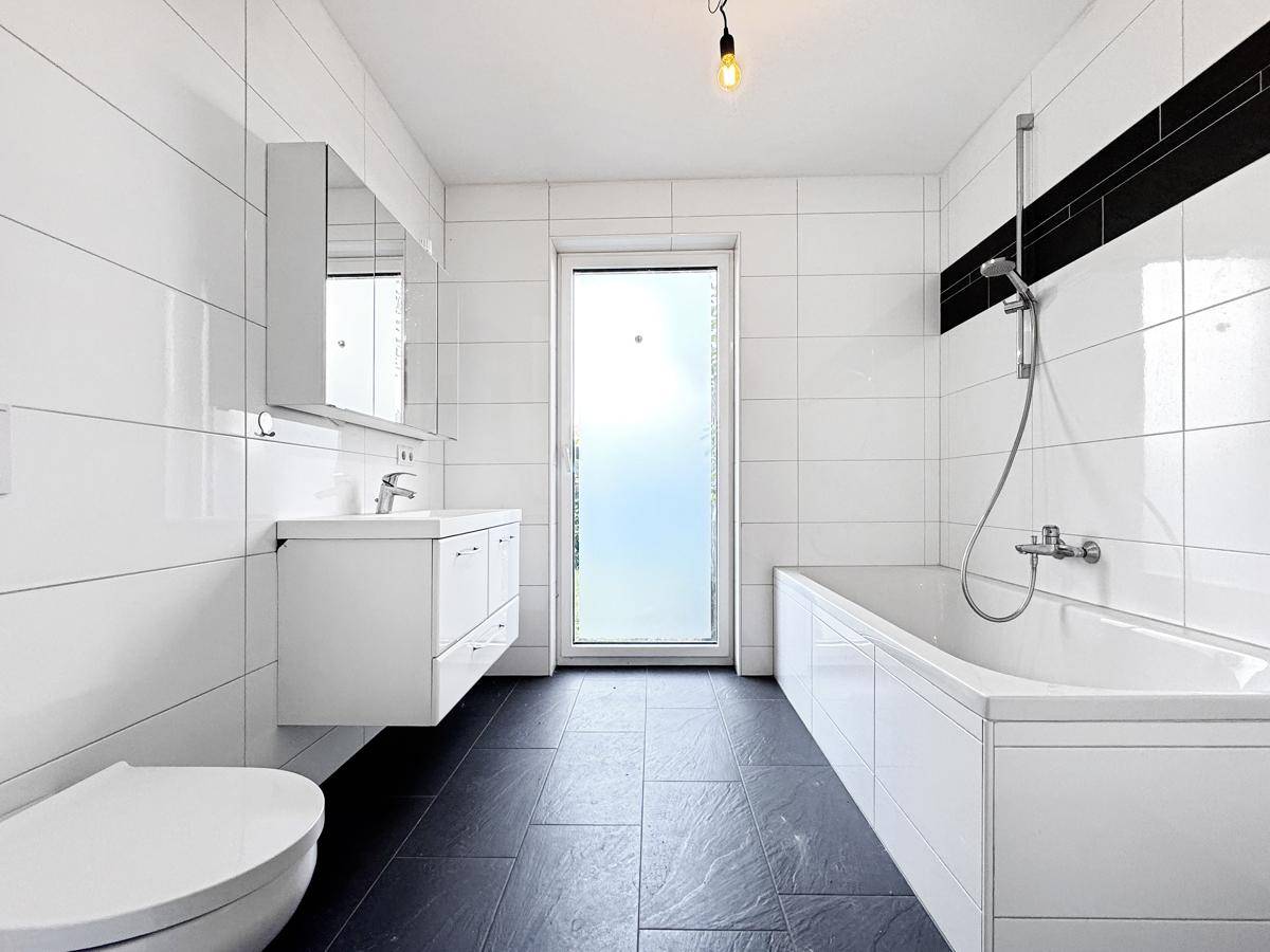 Helles Badezimmer mit Badewanne, Waschtisch, Toilette und Fenster für Tageslicht.