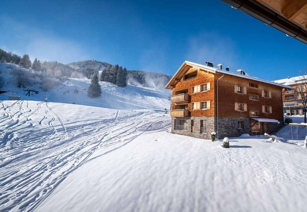 Attraktives Holzhaus mit Schindelfassade direkt an einer schneebedeckten Skipiste gelegen.