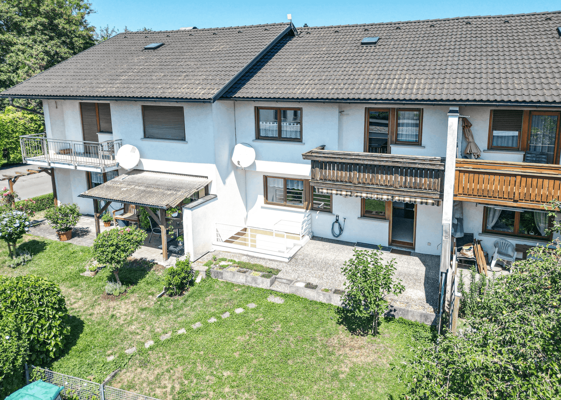 Luftaufnahme der Hausrückseite mit Garten, Terrasse und Balkonen.