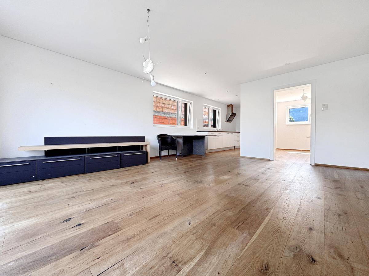 Geräumiger Wohnbereich mit Holzboden, weiß gestrichenen Wänden und Blick auf die Küche.