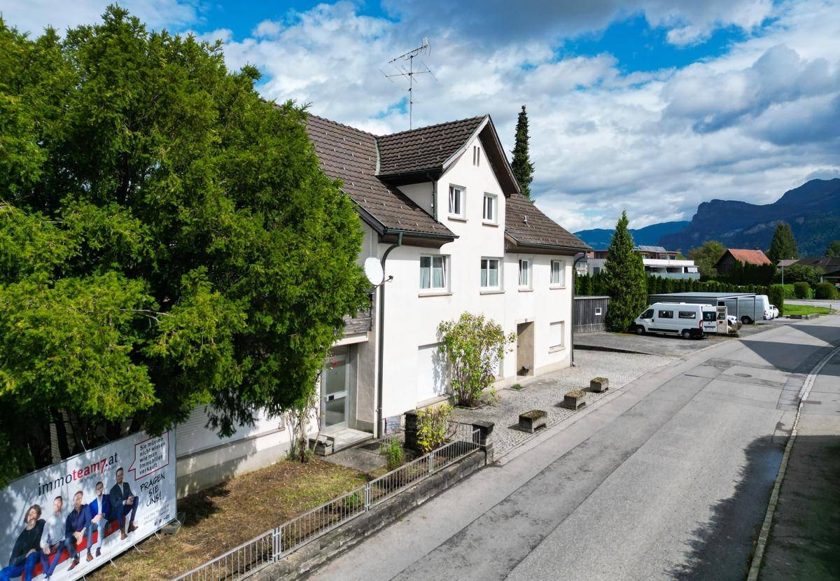 Seitenansicht des Hauses mit großem Baum im Vordergrund und gepflasterter Zufahrt.