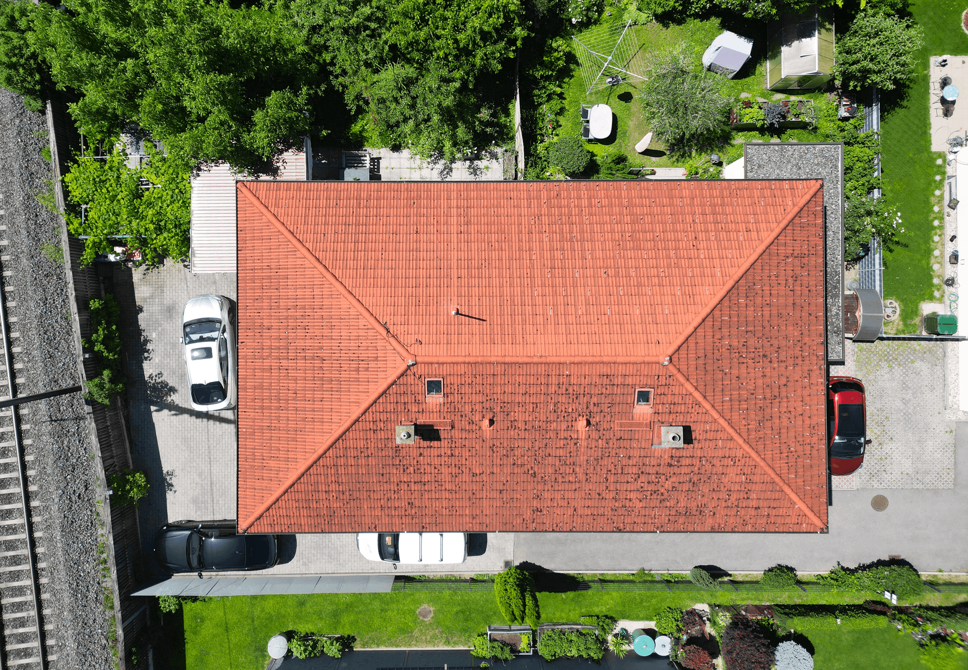 Dachansicht des Hauses mit rotem Ziegeldach, umgeben von Gärten und Bahngleisen, in ruhiger Lage.