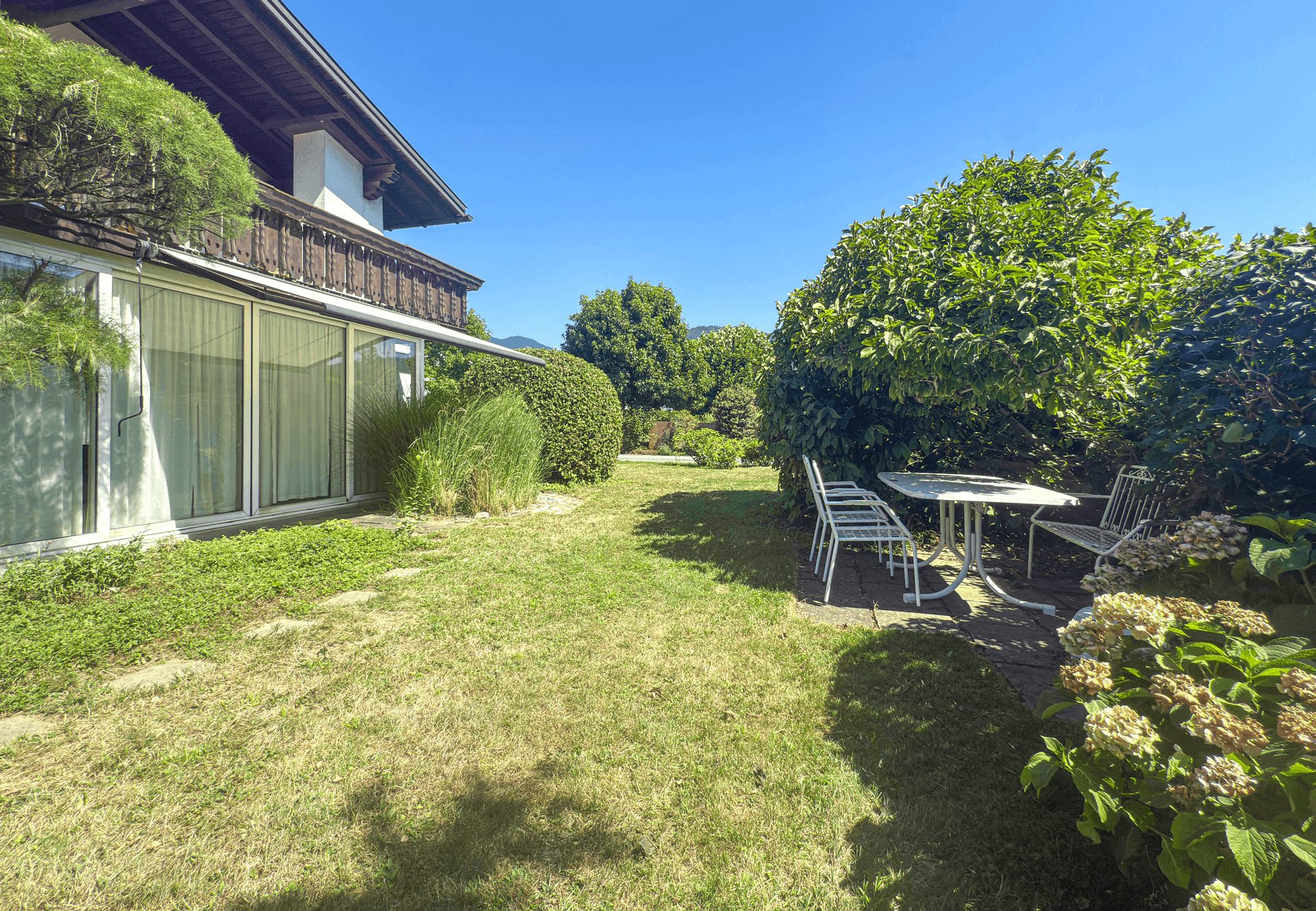 Großer Garten mit Rasen, Terrasse und Blick auf das Haus und die Umgebung.
