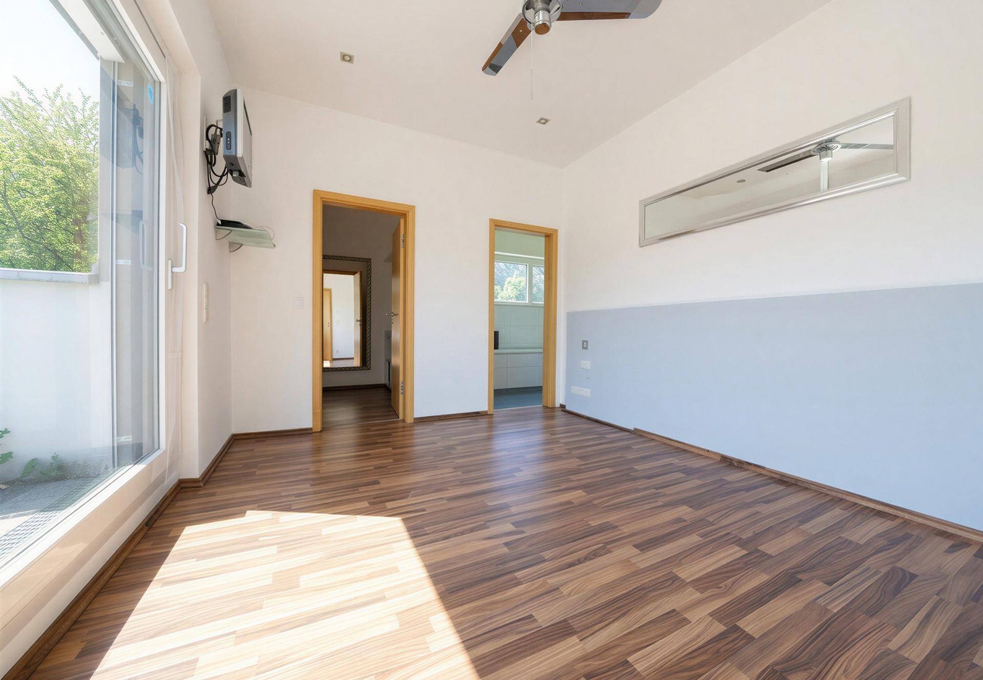 Heller Raum mit Zugang zu einer Terrasse und dunklem Laminatboden, ideal als Schlafzimmer.