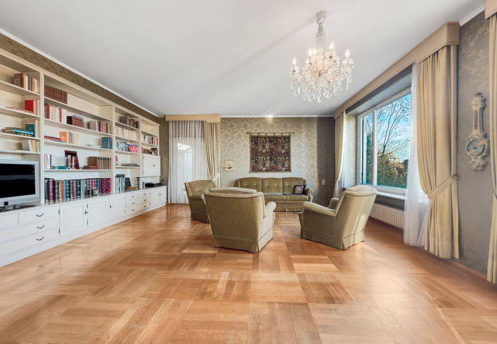 Elegantes Wohnzimmer mit eingebautem Bücherregal, Parkettboden und klassischem Kronleuchter.