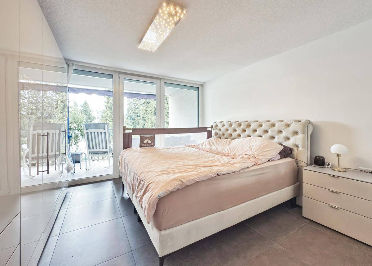 Schlafzimmer mit Doppelbett, Zugang zum Balkon und Fliesenboden.