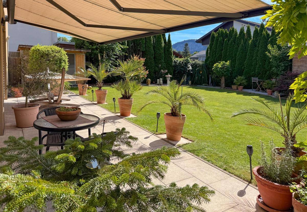 Sonniger Terrassenbereich mit Gartenmöbeln, Pflanzen und Blick auf den gepflegten Garten.