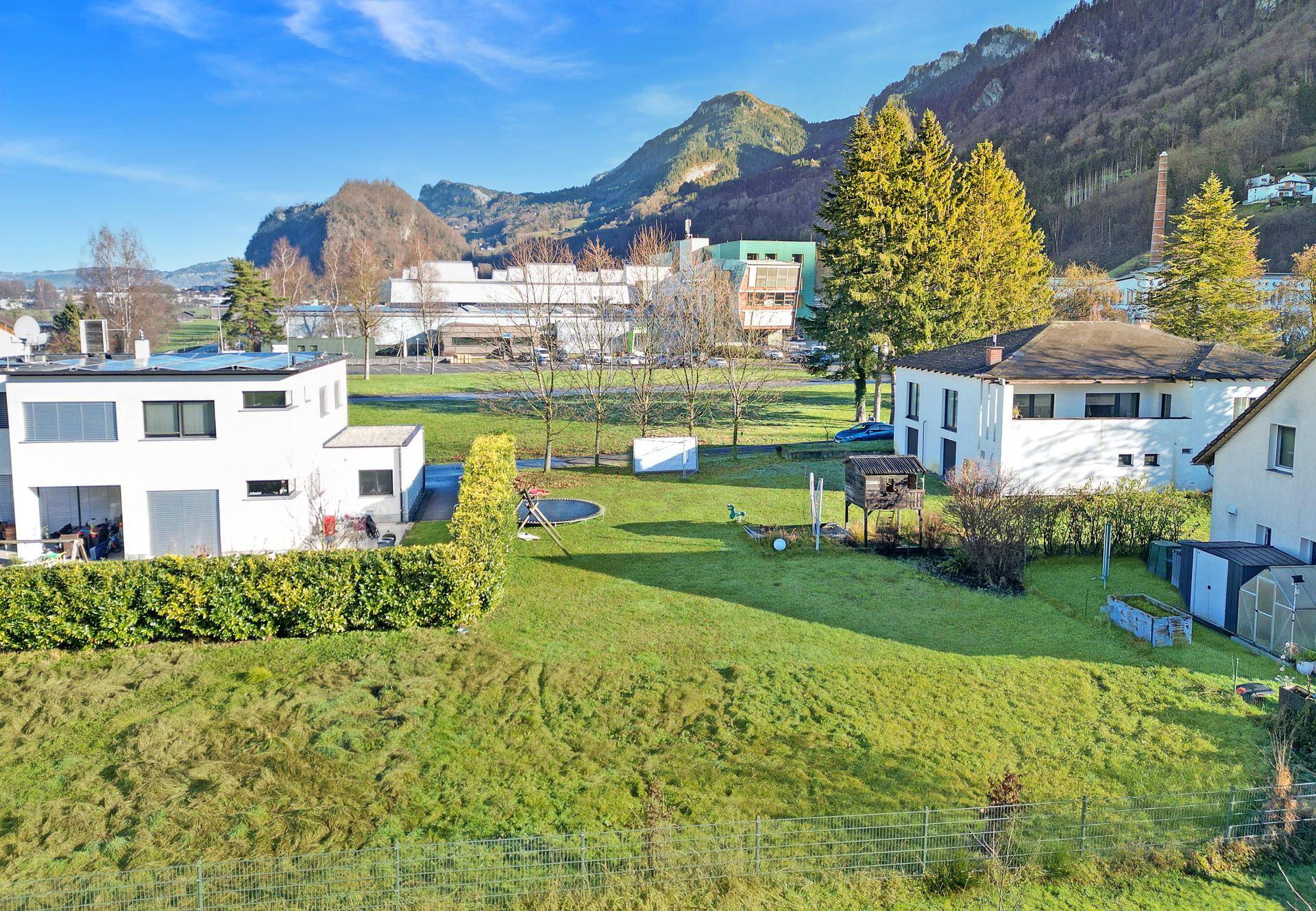 Weitläufige Luftaufnahme der Wohngegend mit grünen Wiesen und Bergen im Hintergrund.