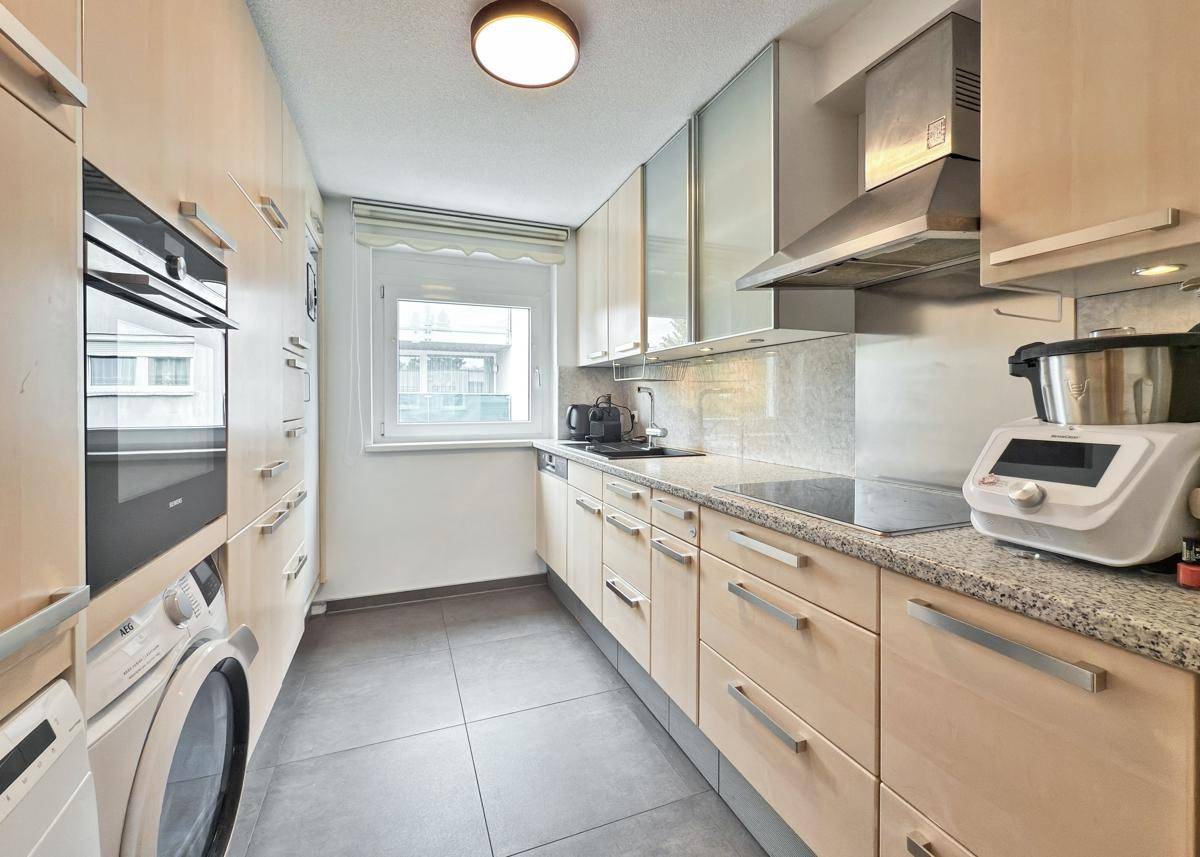 Funktionale Küche mit hellen Holzschränken, Granitarbeitsplatte und integrierten Geräten.