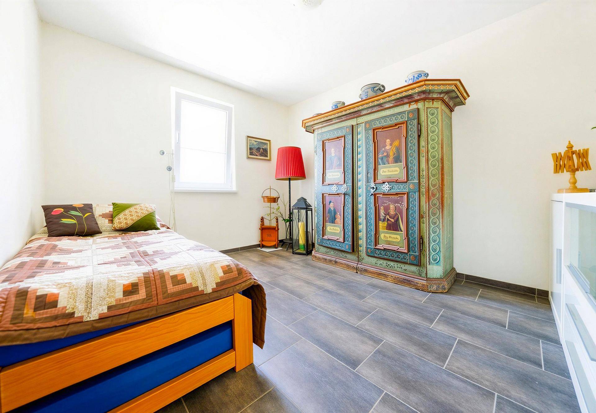 Kinderzimmer oder Gästezimmer mit Einzelbett, farbenfrohem Schrank und Fliesenboden.