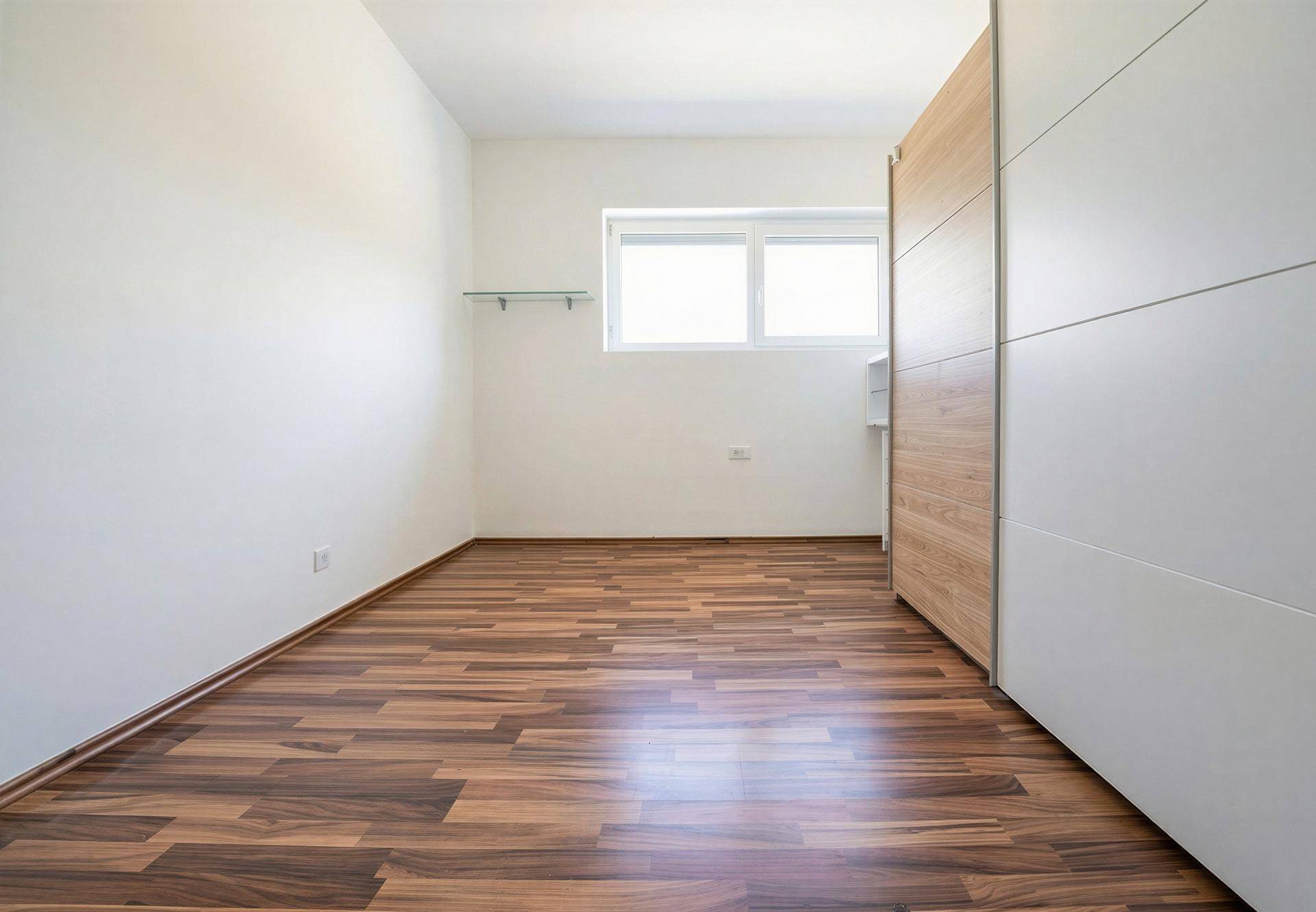 Helles Schlafzimmer mit Fenster, Laminatboden und integriertem Kleiderschrank.