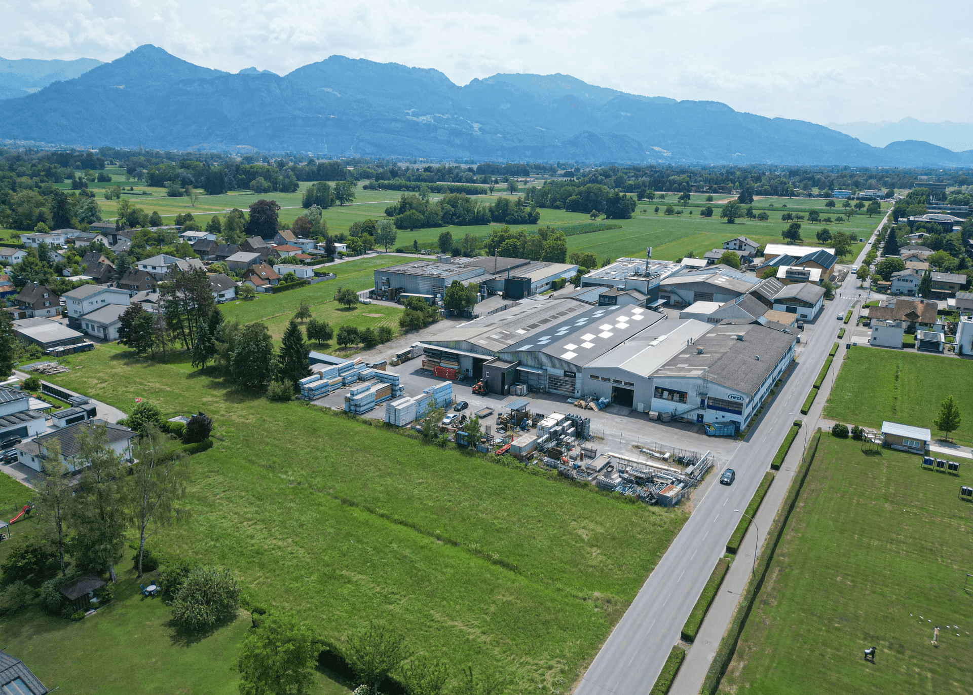 Panoramablick aus der Luft auf das Grundstück, umgeben von Gewerbe und Wohngebieten mit Alpenkulisse.
