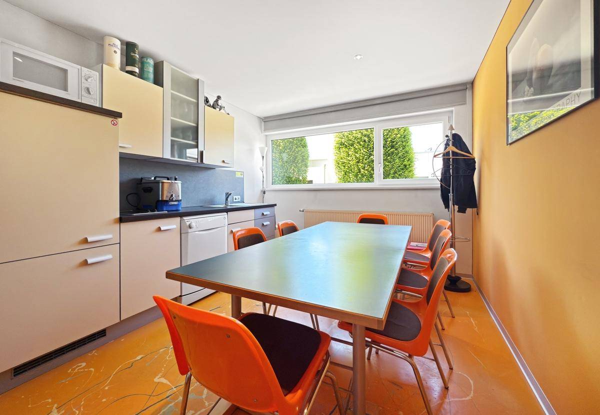 Funktionale Küche mit Essbereich, orangefarbenen Stühlen und einem Fenster mit Blick ins Grüne.