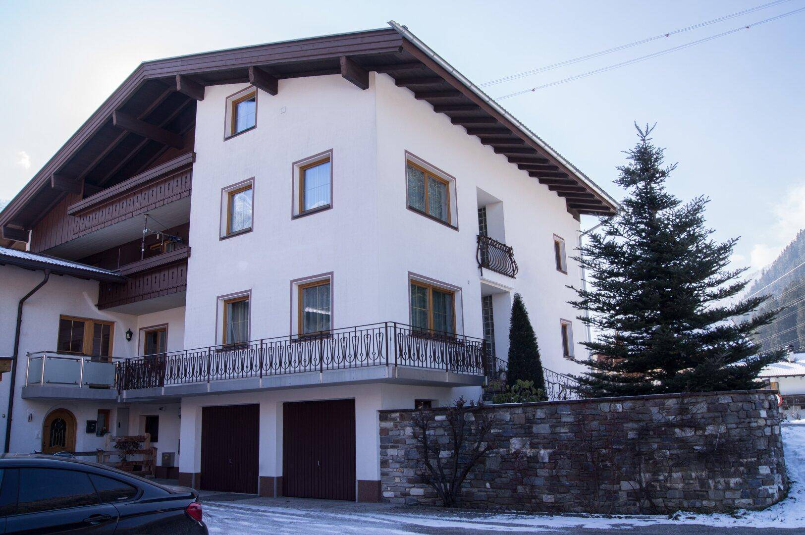 Charmantes Haus mit weißer Fassade, Holzbalkonen und integrierter Garage in alpiner Umgebung.