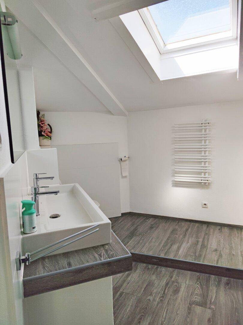 Helles Badezimmer mit Dachfenster, modernem Waschbecken und Holzbodenoptik.