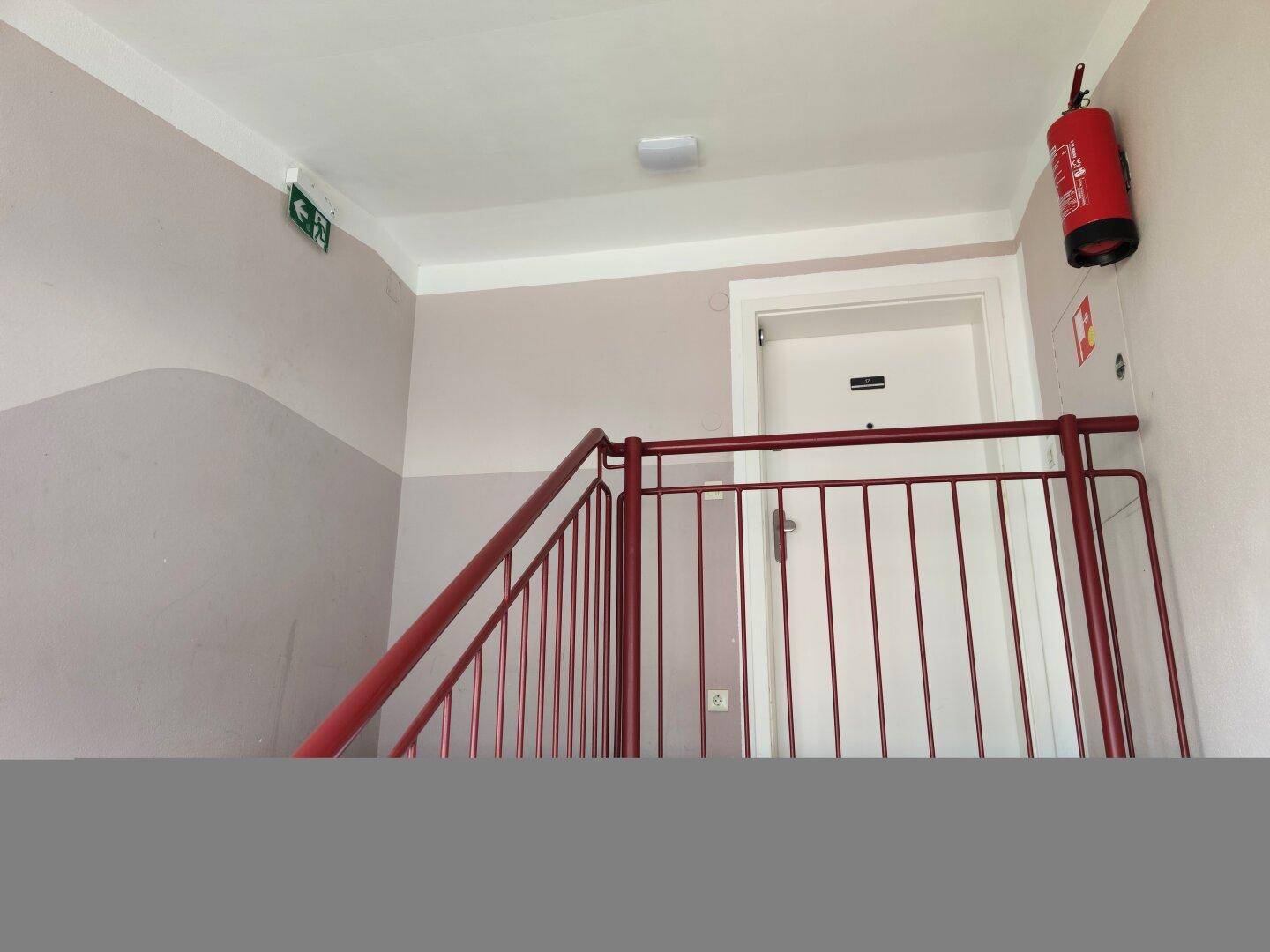 Treppenhaus mit rotem Geländer, weißer Tür und Brandschutzvorrichtungen.