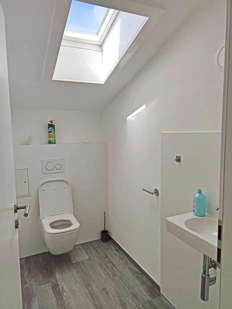 Helles Gäste-WC mit wandhängender Toilette, kleinem Waschbecken und Dachfenster.