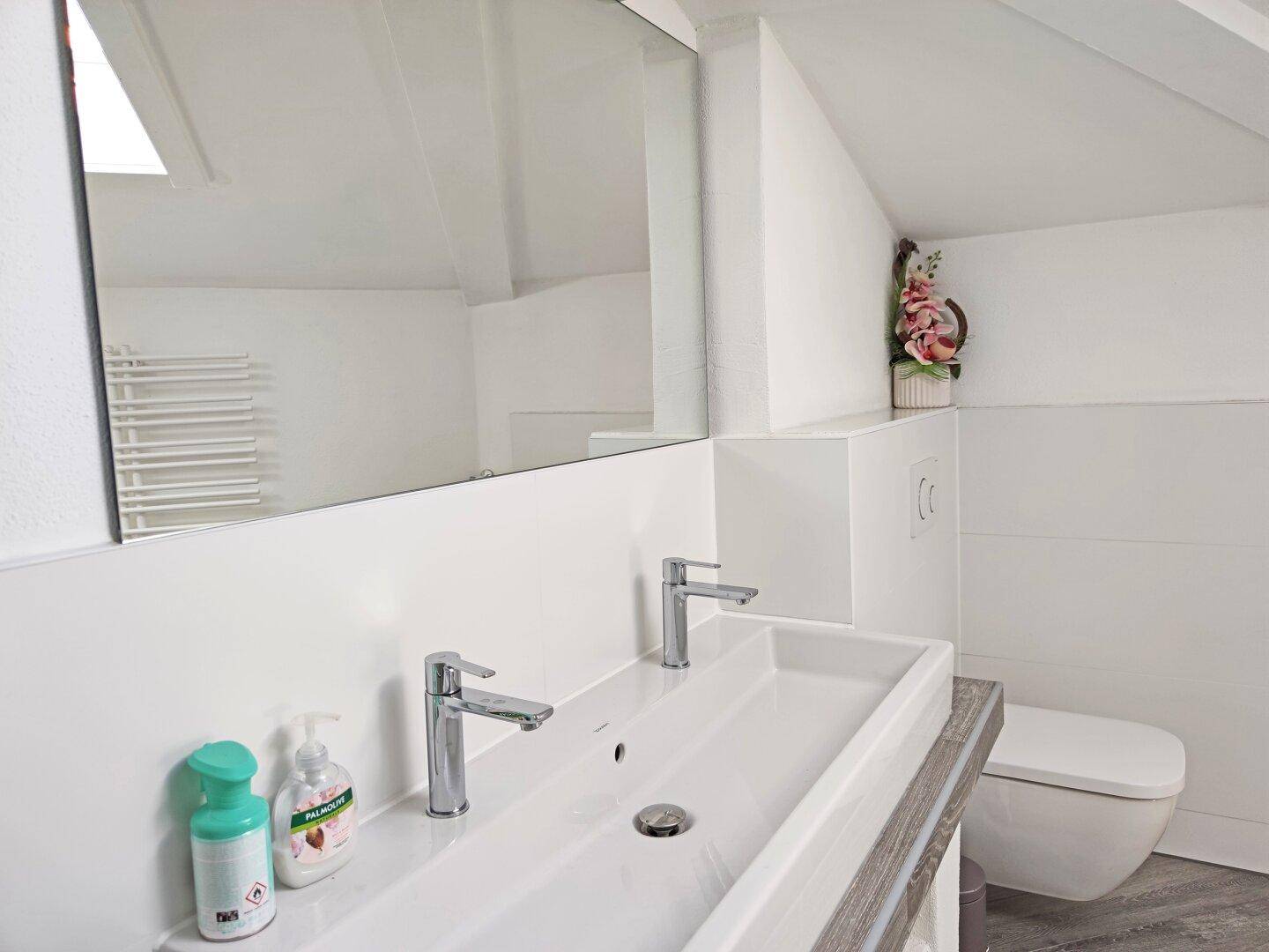 Modernes Badezimmer mit Doppelwaschbecken, großem Spiegel und wandhängendem WC unter Dachschräge.