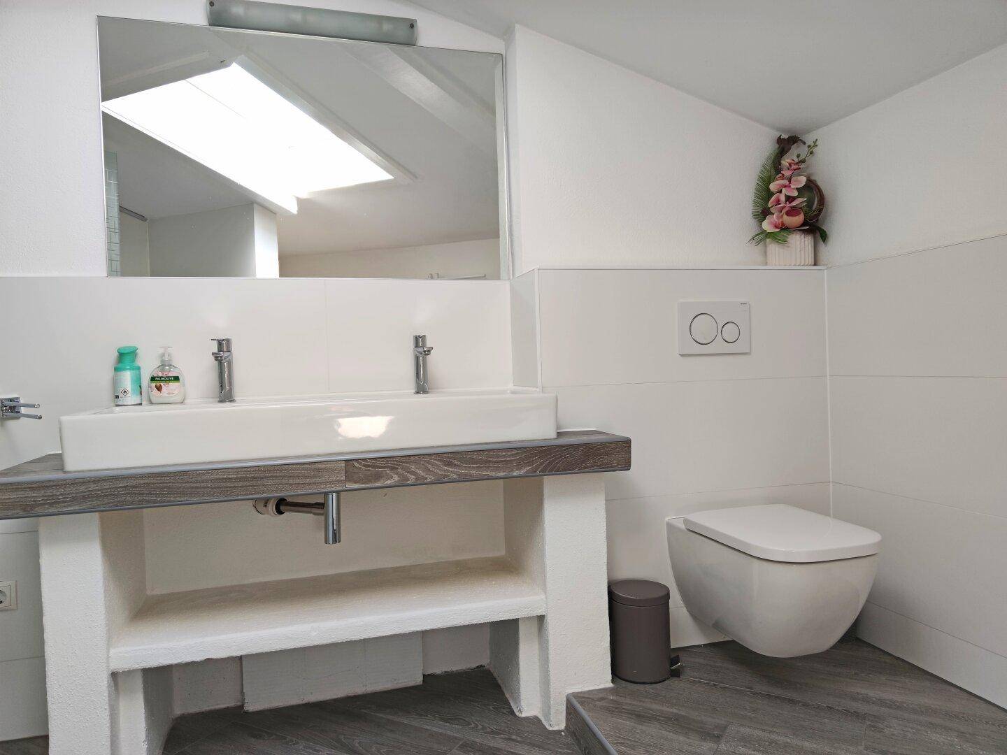 Modernes Badezimmer mit Doppelwaschbecken, großem Spiegel und wandhängendem WC unter Dachschräge.
