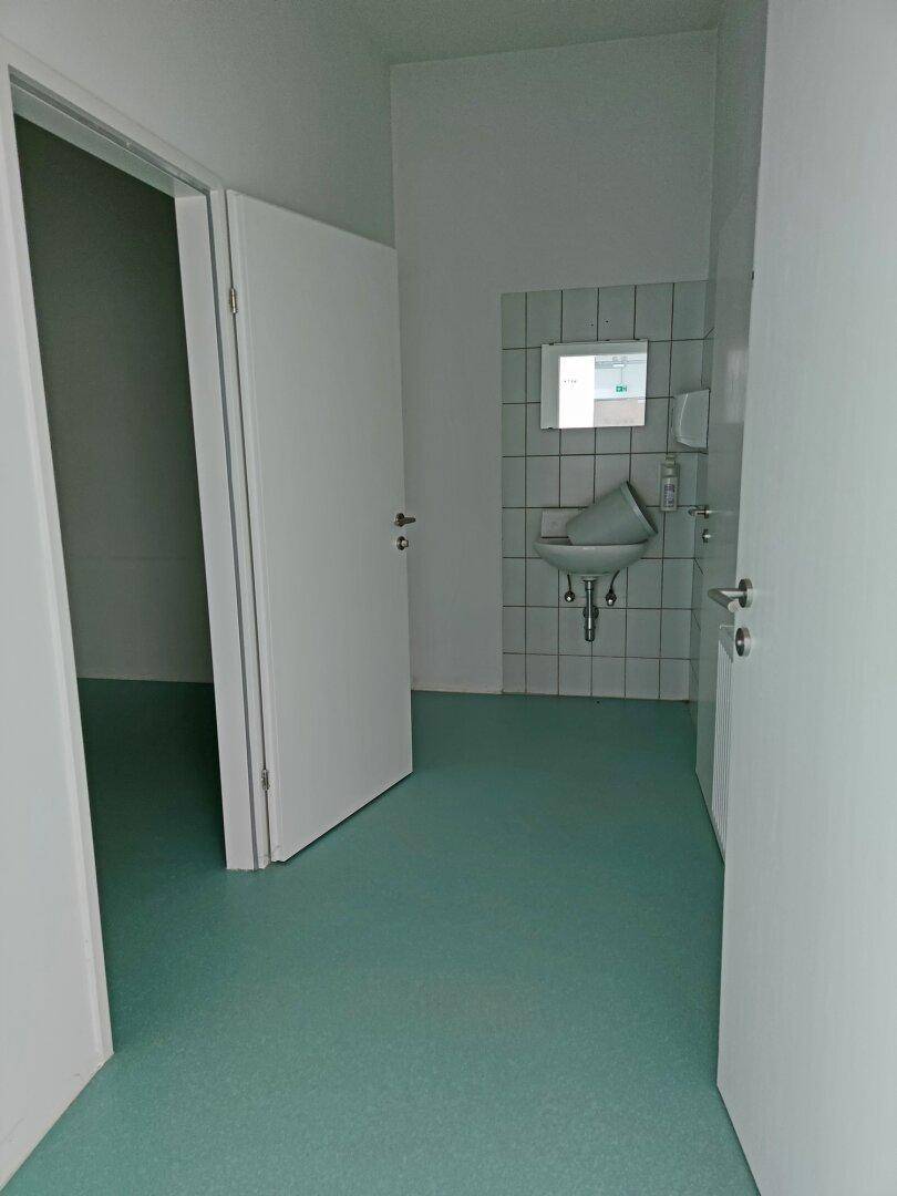 Kleiner, funktionaler Waschraum mit Waschbecken, Spiegel und weiß gefliesten Wänden.