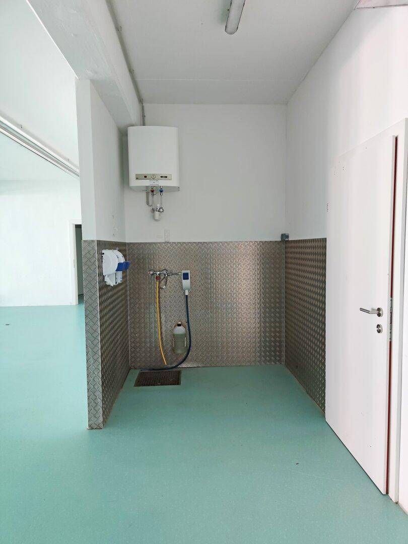 Funktionaler Hauswirtschaftsraum mit Warmwasserbereiter, Metallverkleidung und Bodenablauf.