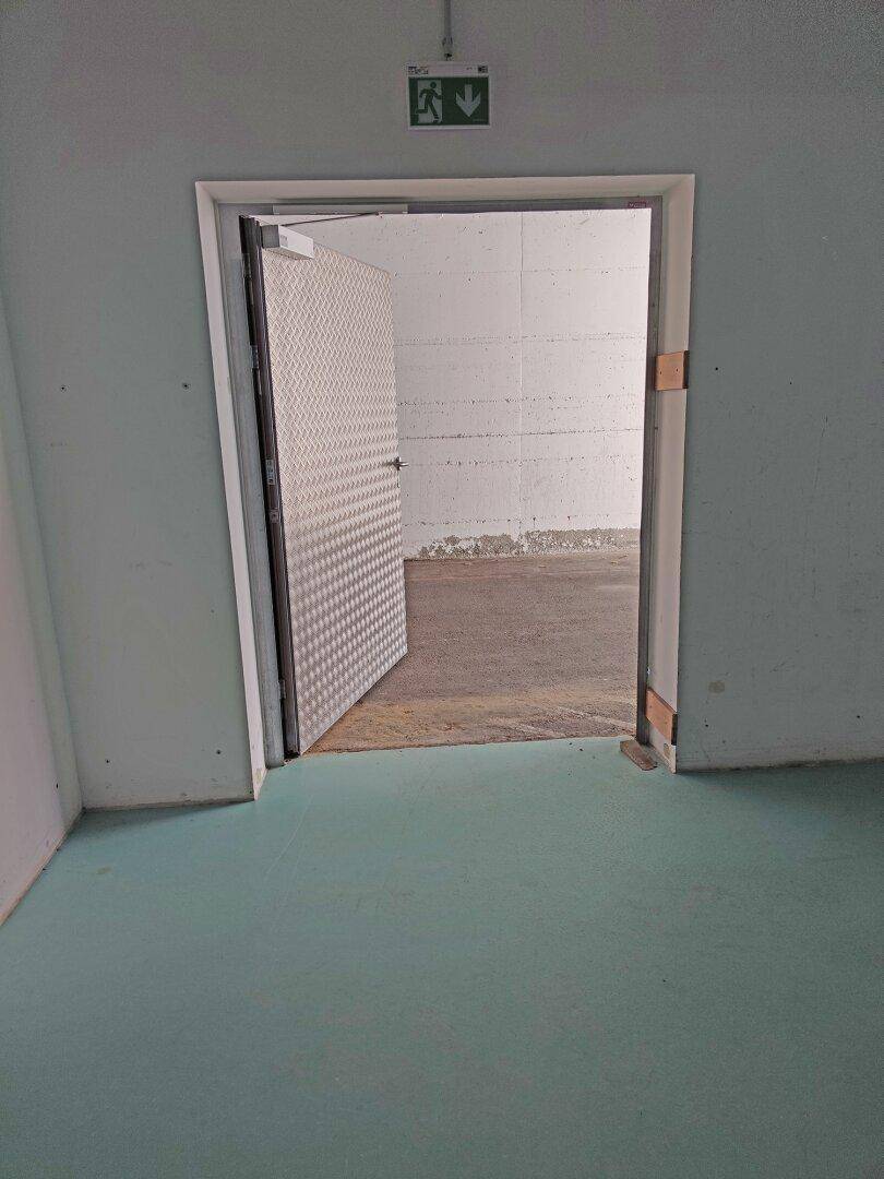 Offene Metalltür führt in einen weiteren Bereich, möglicherweise einen Lagerraum oder Keller.