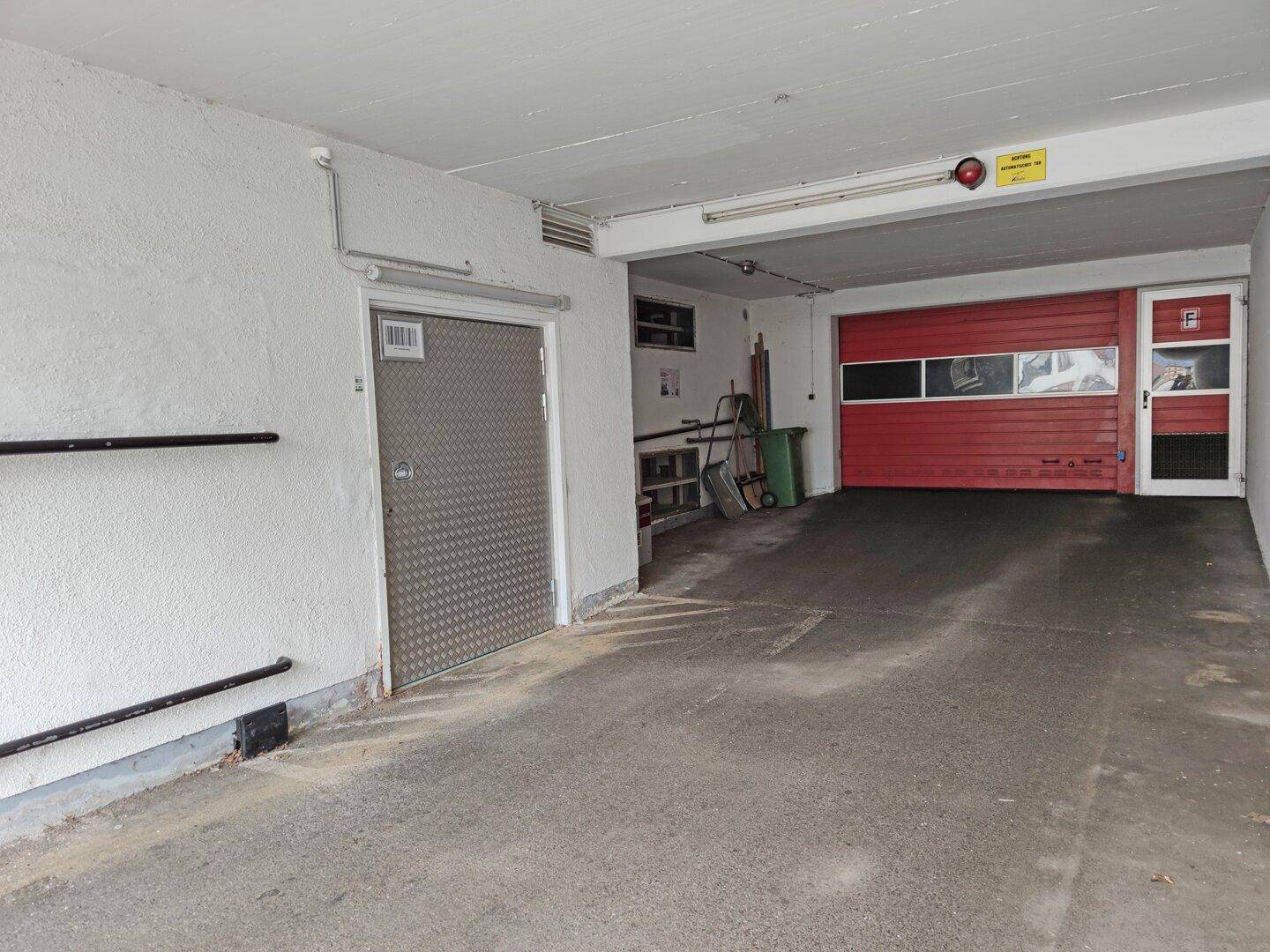 Geräumige Garage oder Lagerfläche mit rotem Rolltor und einer robusten Metalltür.