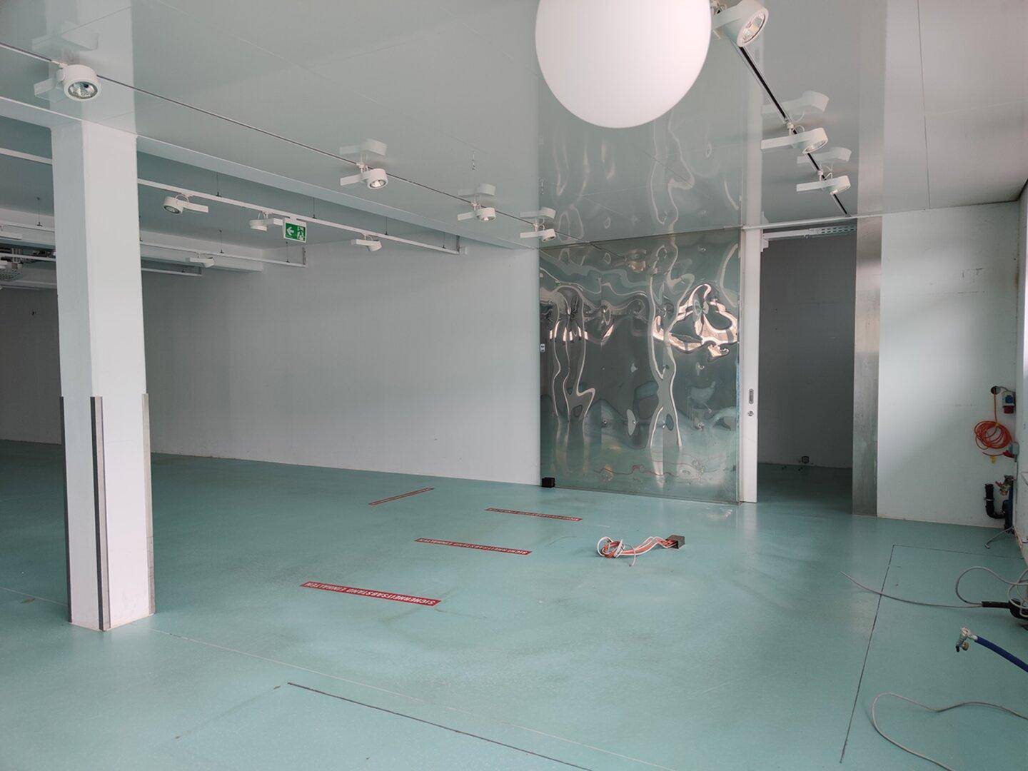 Großer Gewerberaum mit hellblauem Boden, reflektierender Wand und modernen Deckenleuchten.