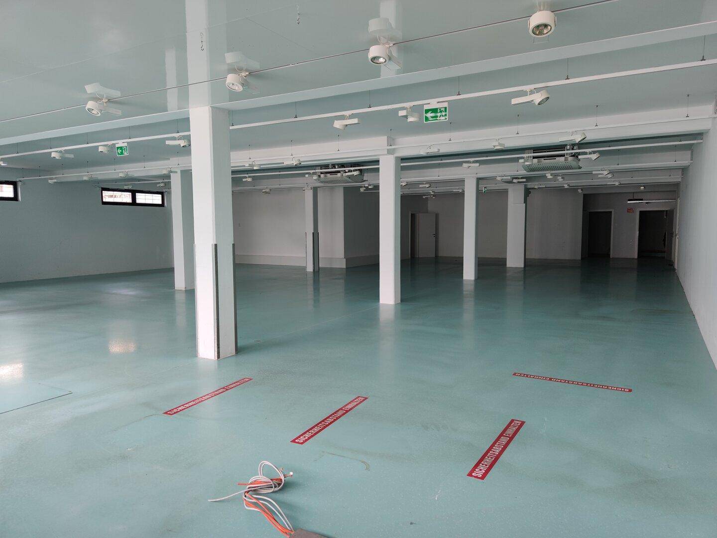 Weitläufiger Gewerberaum mit vielen Säulen, Deckenleuchten und roten Markierungen auf dem Boden.