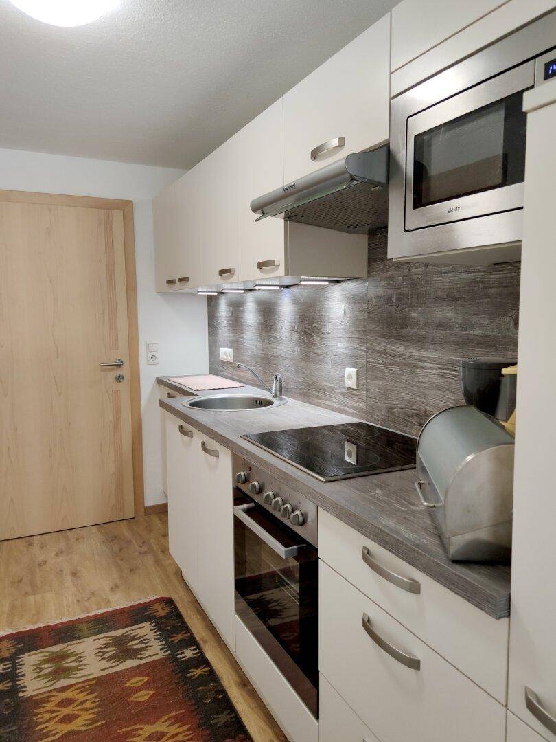 Moderne Küchenzeile mit integrierten Geräten, Spüle und Holzoptik-Arbeitsplatte.