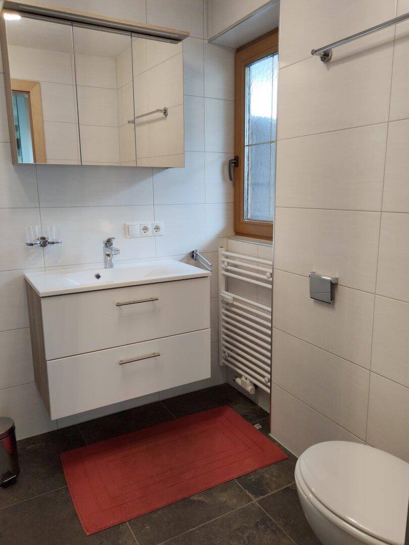 Helles Badezimmer mit Waschtisch, WC, Fenster und beheiztem Handtuchhalter.