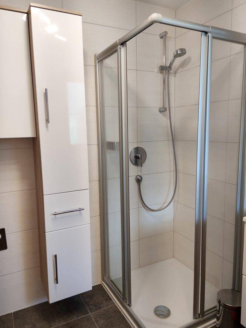 Modernes Badezimmer mit Duschkabine und weißen Hochglanzschränken für Stauraum.