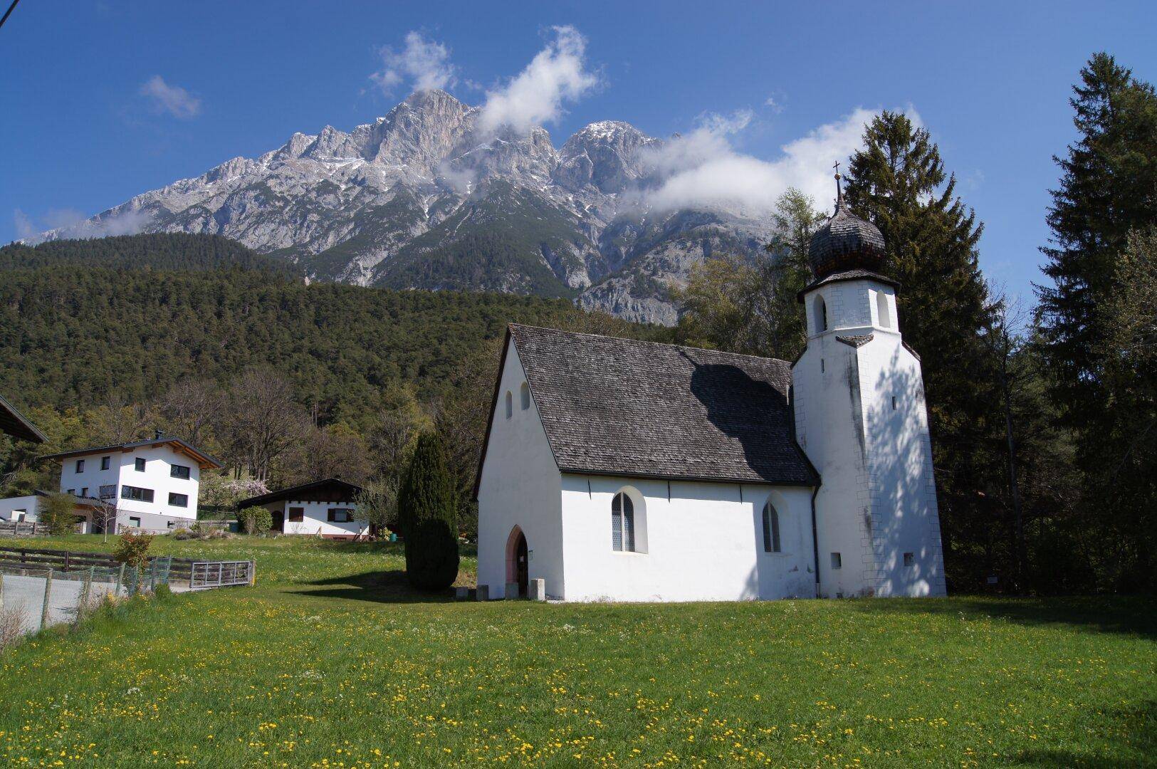 Malerische Kapelle in grüner Wiesenlandschaft mit imposantem Bergpanorama im Hintergrund.
