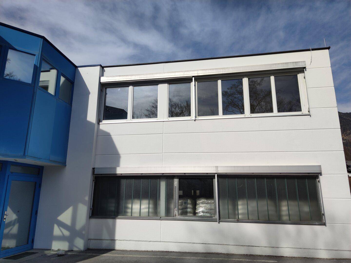Moderne Gebäudefassade mit blauen und weißen Elementen, großen Fenstern und Rollläden.