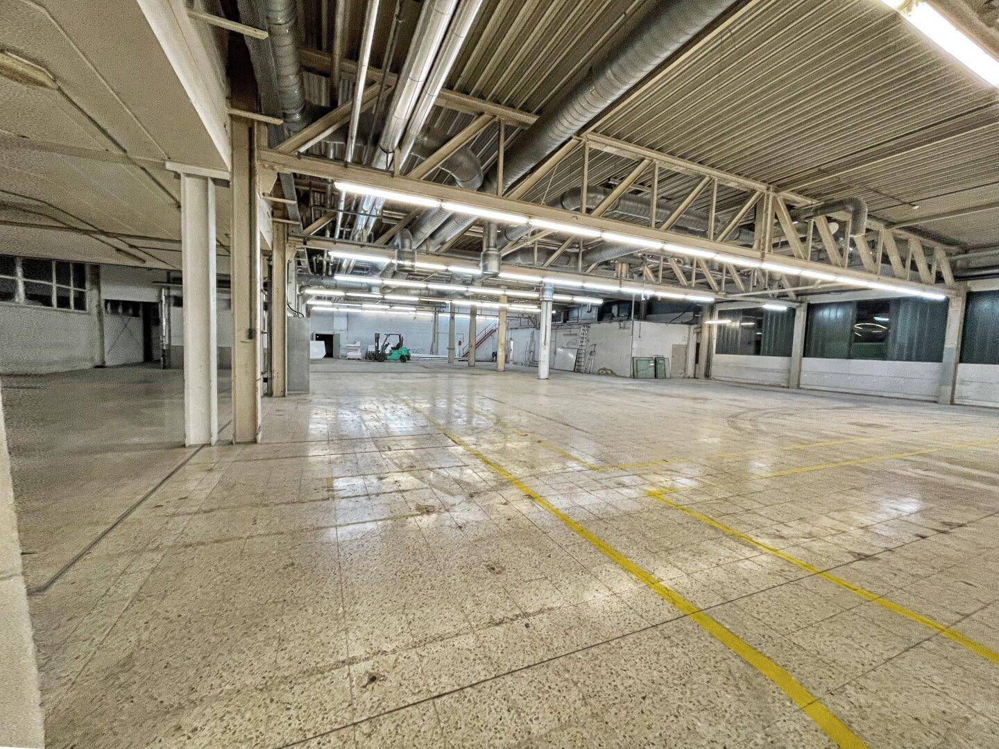 Weitläufiger Industriebereich mit hohen Decken, sichtbaren Rohren und einem Gabelstapler im Hintergrund.