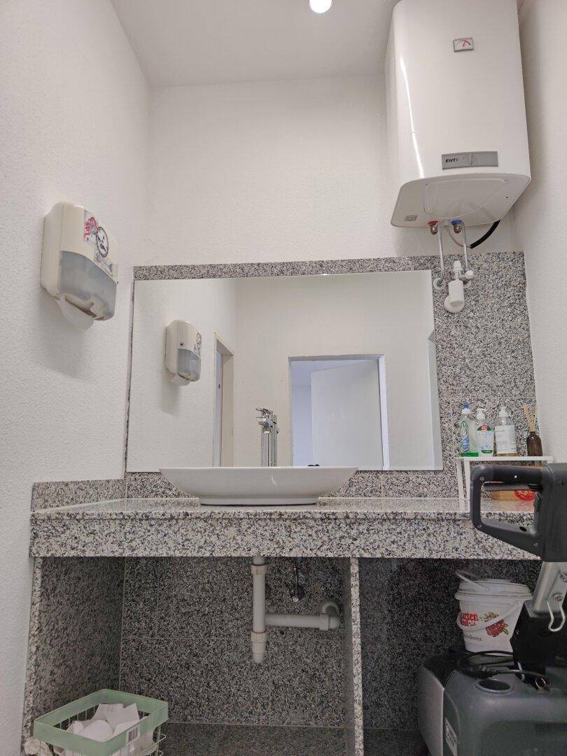 Badezimmer mit Waschbecken, großem Spiegel und einem Warmwasserboiler an der Wand.