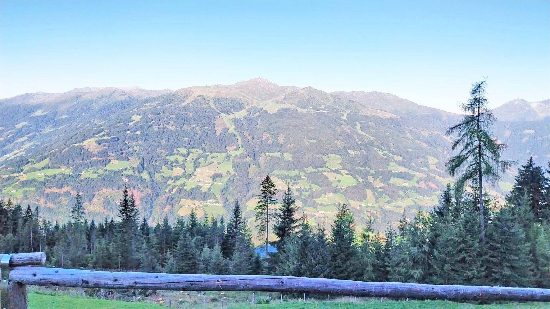 Holzzaun im Vordergrund mit weitem Blick auf die sanften Hügel und bewaldeten Berge.