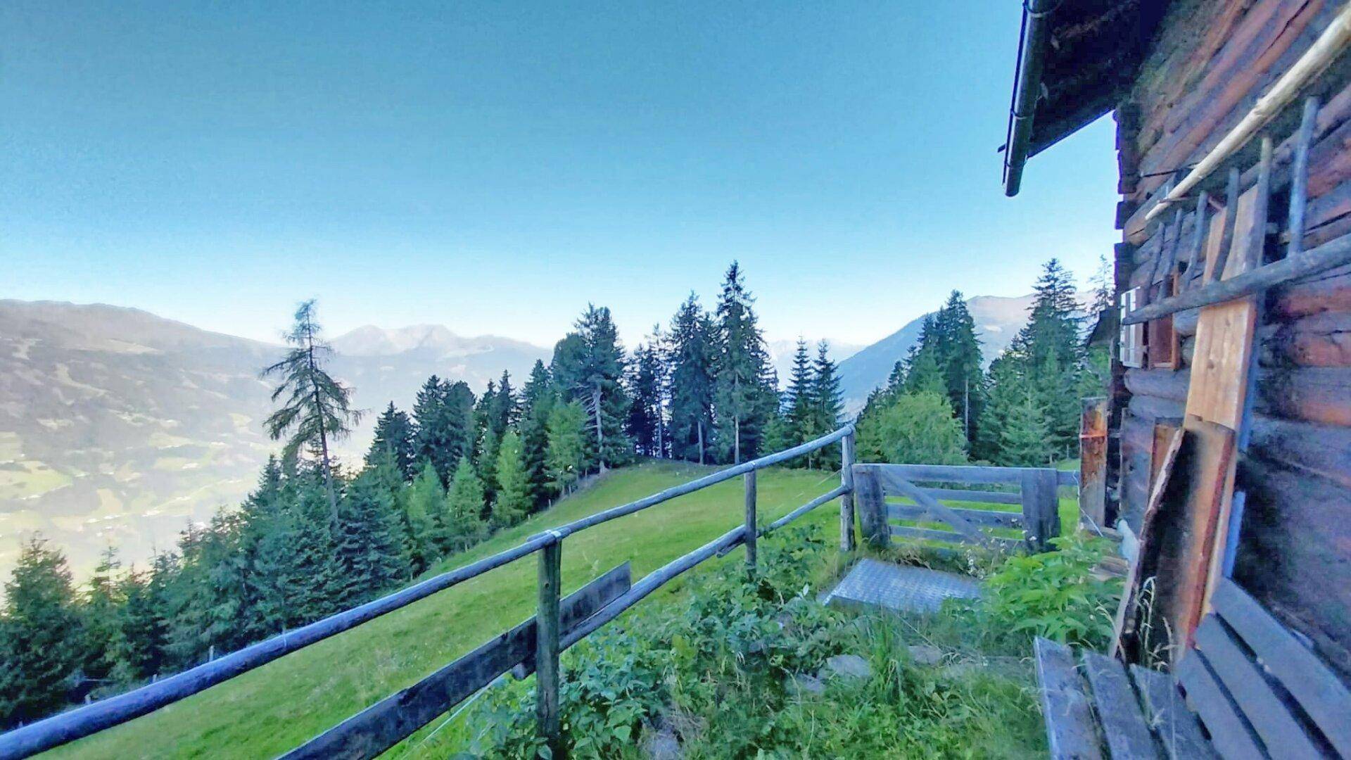 Rustikaler Holzzaun und Bank mit Panoramablick auf die bewaldeten Berge und das Tal.